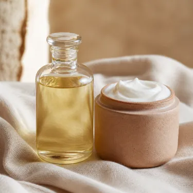 A bottle of massage oil and a jar of deep tissue massage cream side by side on folded linen in a treatment room.