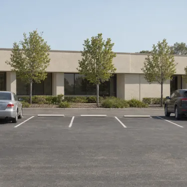 A quiet surface car park beside a low office building in flat daylight.