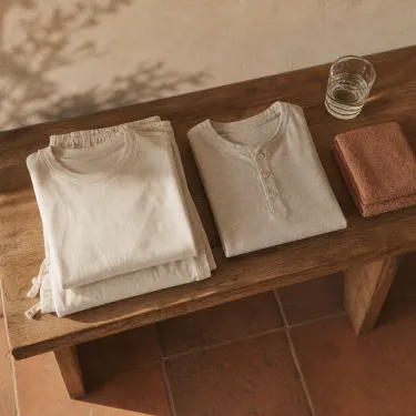 Loose comfortable clothing folded on a bench beside a glass of water and a towel